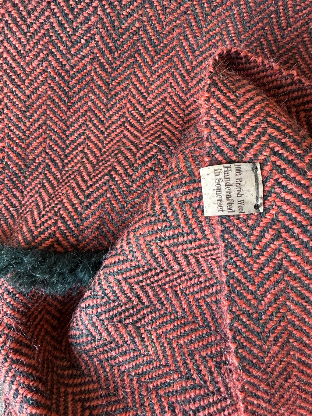Close-up of a herringbone-patterned fabric with a label saying 100% British wool, handcrafted in Somerset
