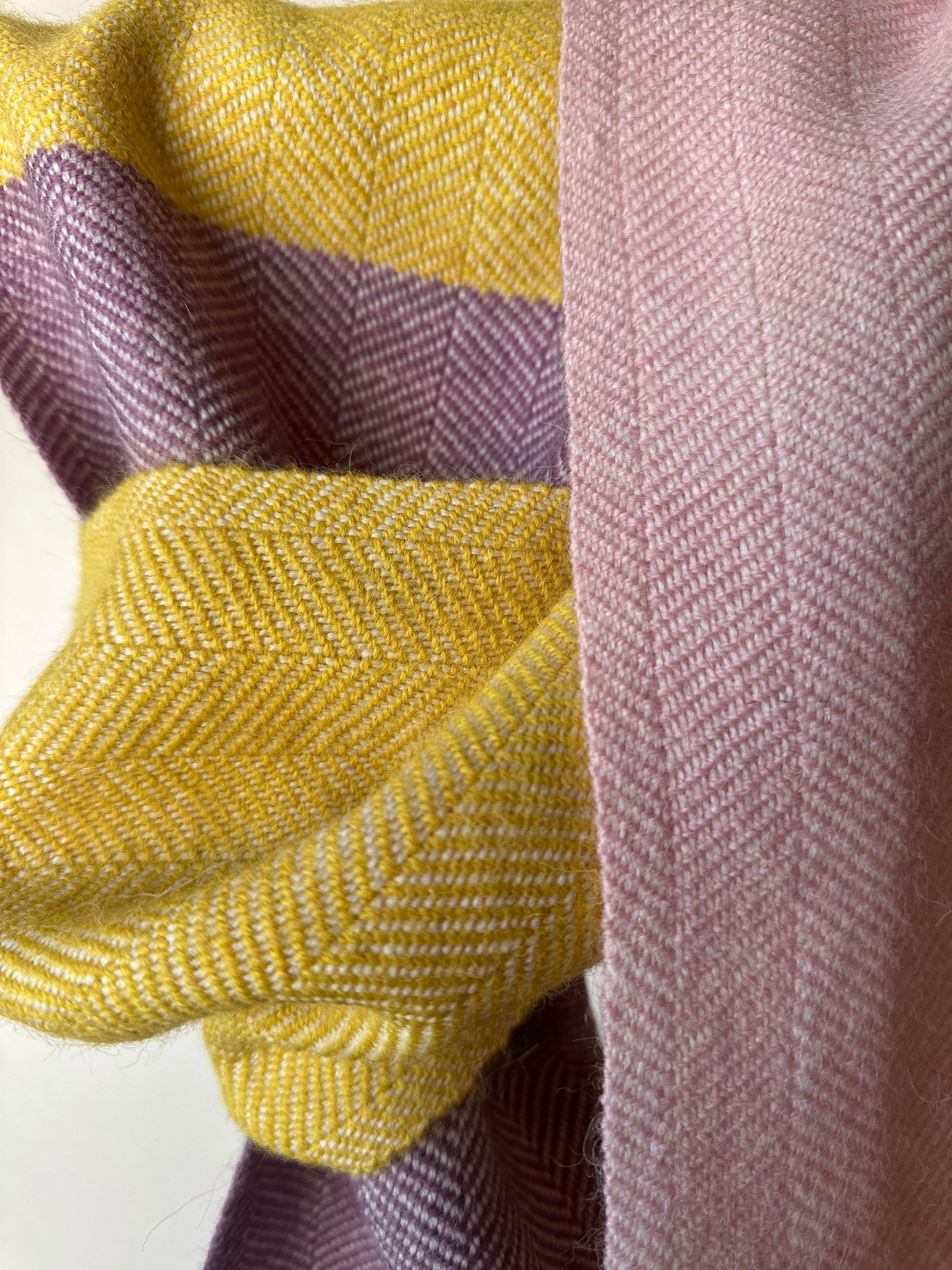 Close-up of fabric with a herringbone pattern in yellow, pink and purple.