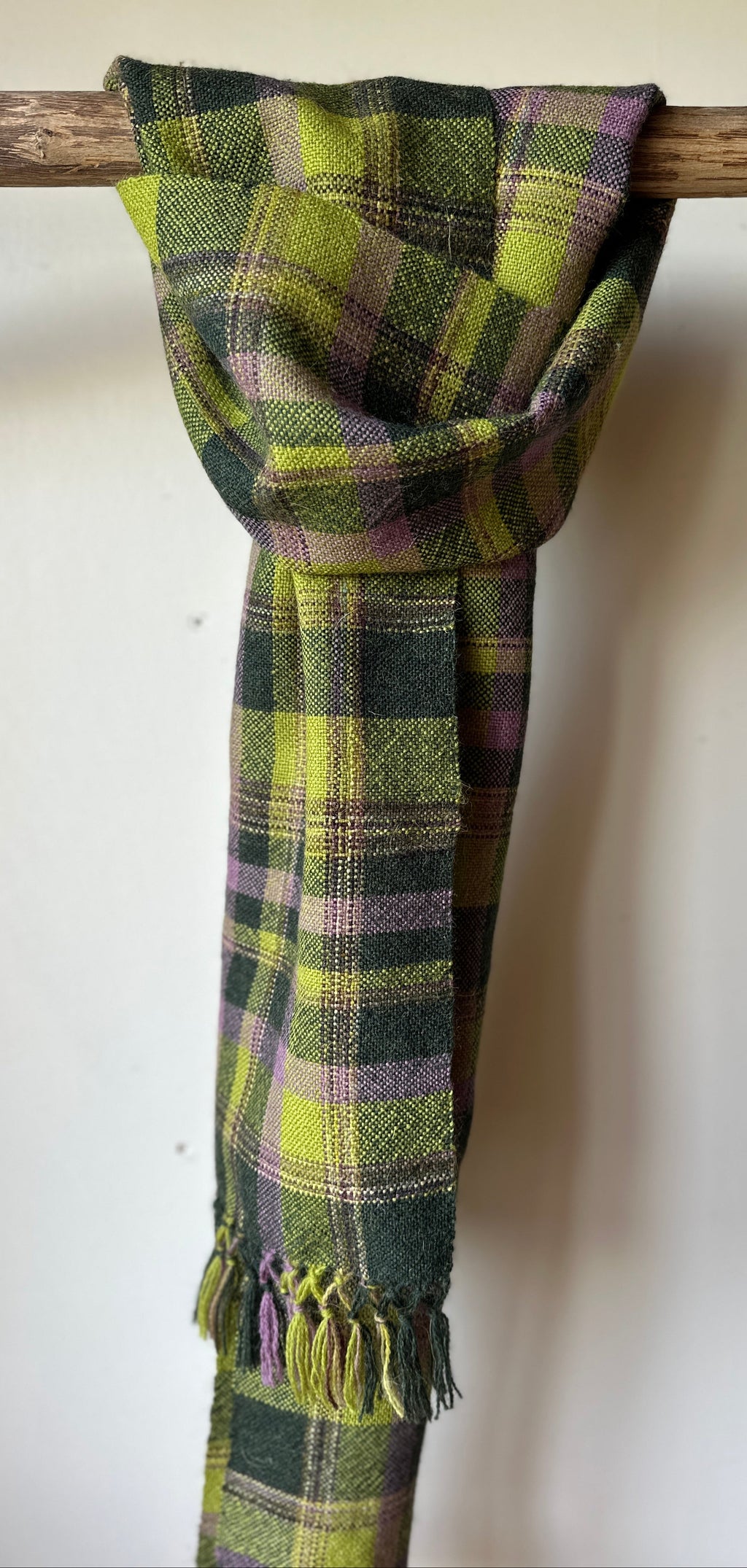 Green and purple plaid scarf draped over a wooden stick against a white wall.