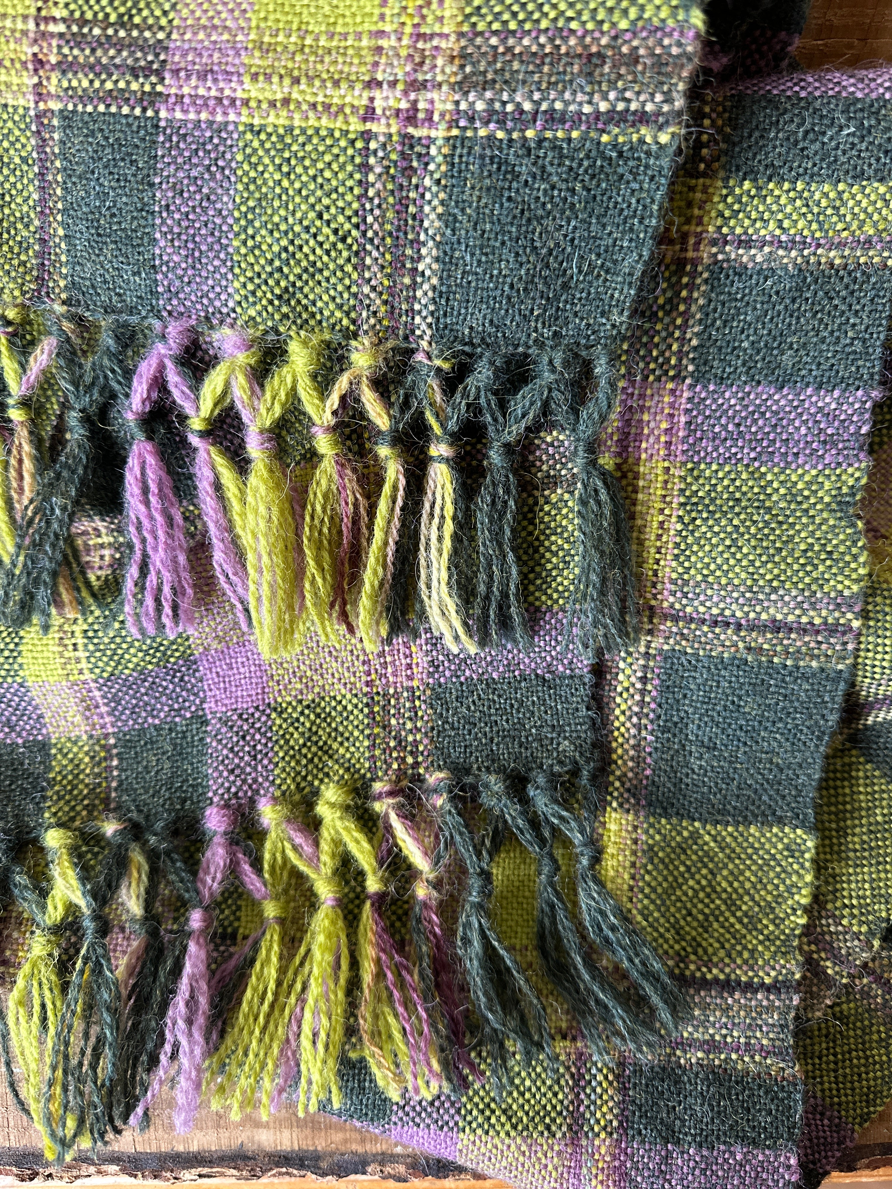 Close-up of a plaid fabric with tassels in green and purple.