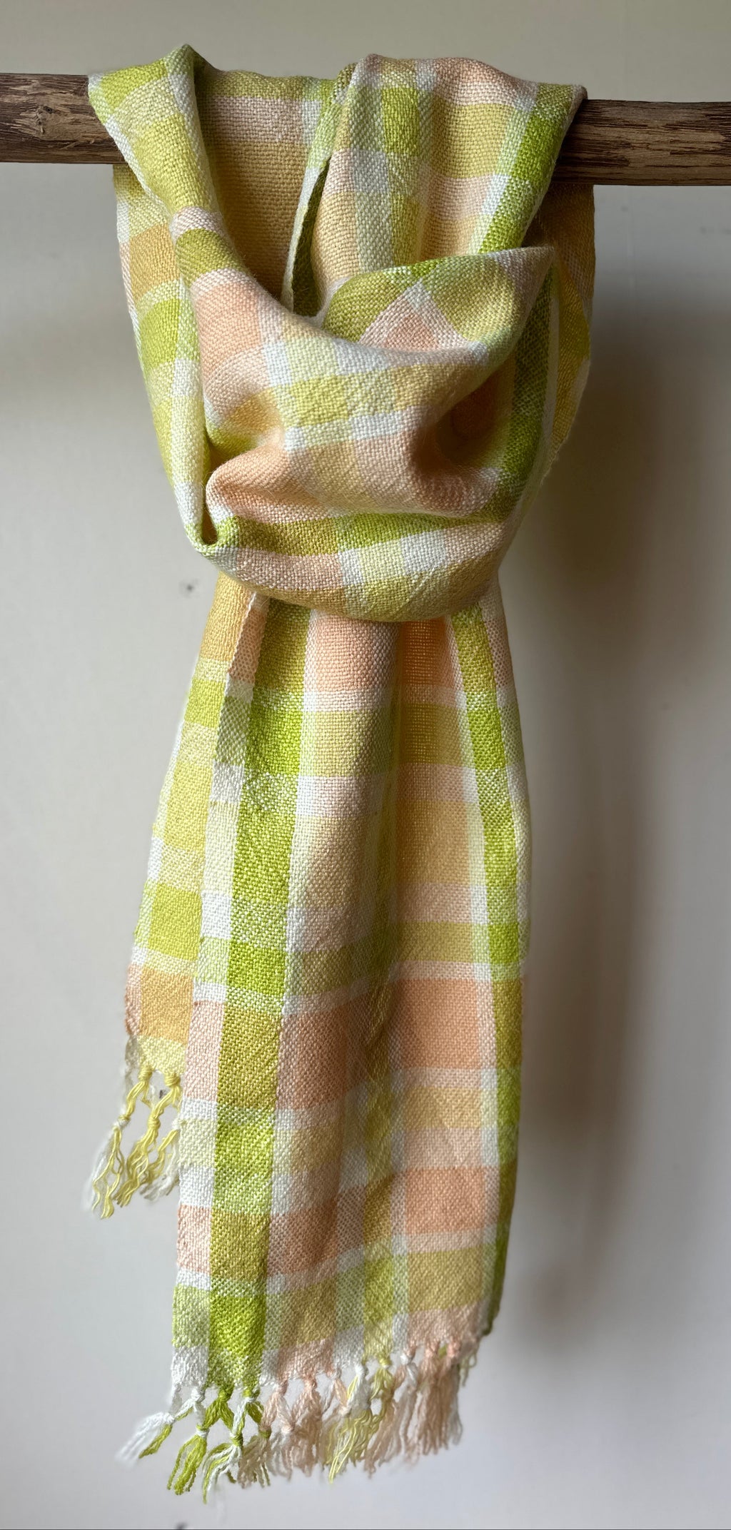 Plaid scarf with green and orange pattern draped over a wooden branch on a white background