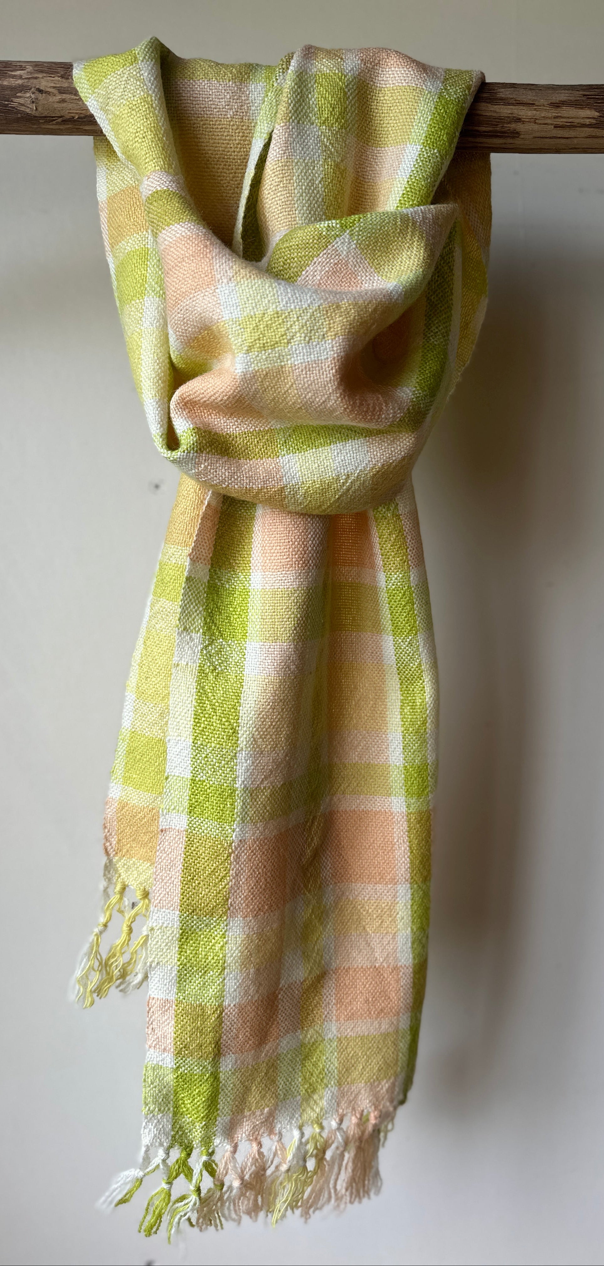 Plaid scarf with green and orange pattern draped over a wooden branch on a white background